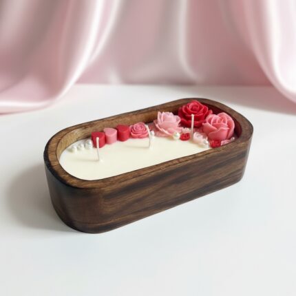 A high-end product photo of a handcrafted boat-shaped wooden dough bowl candle by EKAA Candles, featuring three burning wicks, hand-poured soy wax, and detailed pink and red rose embeds with pearls for Valentine's Day.