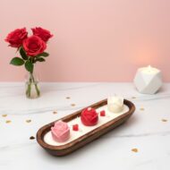 Artisanal rose dough bowl candle by EKAA Candles featuring three hand-poured pink, red, and white roses in a wooden boat-shaped vessel on a marble surface with Valentine's Day decor.