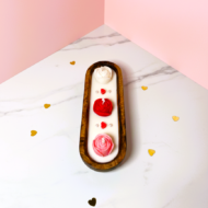 Top-down bird's-eye view of The Rose Hearth candle by EKAA Candles. Three hand-poured wax roses in red, pink, and white are perfectly centered in a wooden dough bowl on a white marble surface with gold heart confetti.