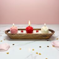 Three-wick lit rose dough bowl candle by EKAA Candles featuring three glowing wax roses in red, pink, and white on a marble table with rose petals and gold confetti.