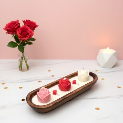 Artisanal rose dough bowl candle by EKAA Candles featuring three hand-poured pink, red, and white roses in a wooden boat-shaped vessel on a marble surface with Valentine's Day decor.