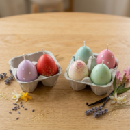 Two eco-friendly gray pulp egg cartons containing 2 and 4 pieces of ekaa candles Easter egg soy wax candles. Designs include polka dots, red matte, teal glitter, and lavender finishes on a light oak wooden background with pink oleander.