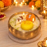 Lit EKAA Mithaas mithai urli candle with laddoo, pedha and kaju katli wax embeds in a gold-toned hammered bowl.